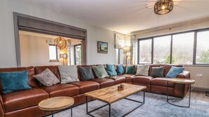 A modern living room with a brown leather sectional sofa, a wooden coffee table, and a round side table. - Garth Hill House (Ambleside)