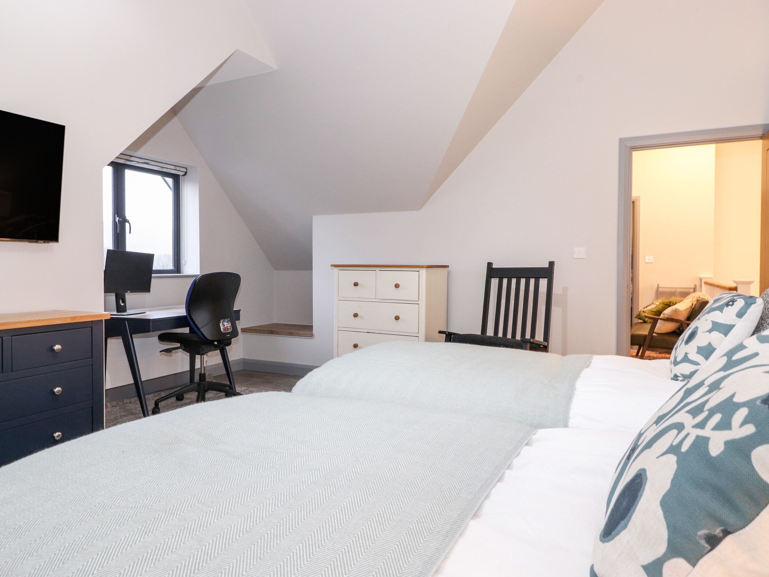 A bedroom with a bed, a desk, a chair, a dresser, and a TV.