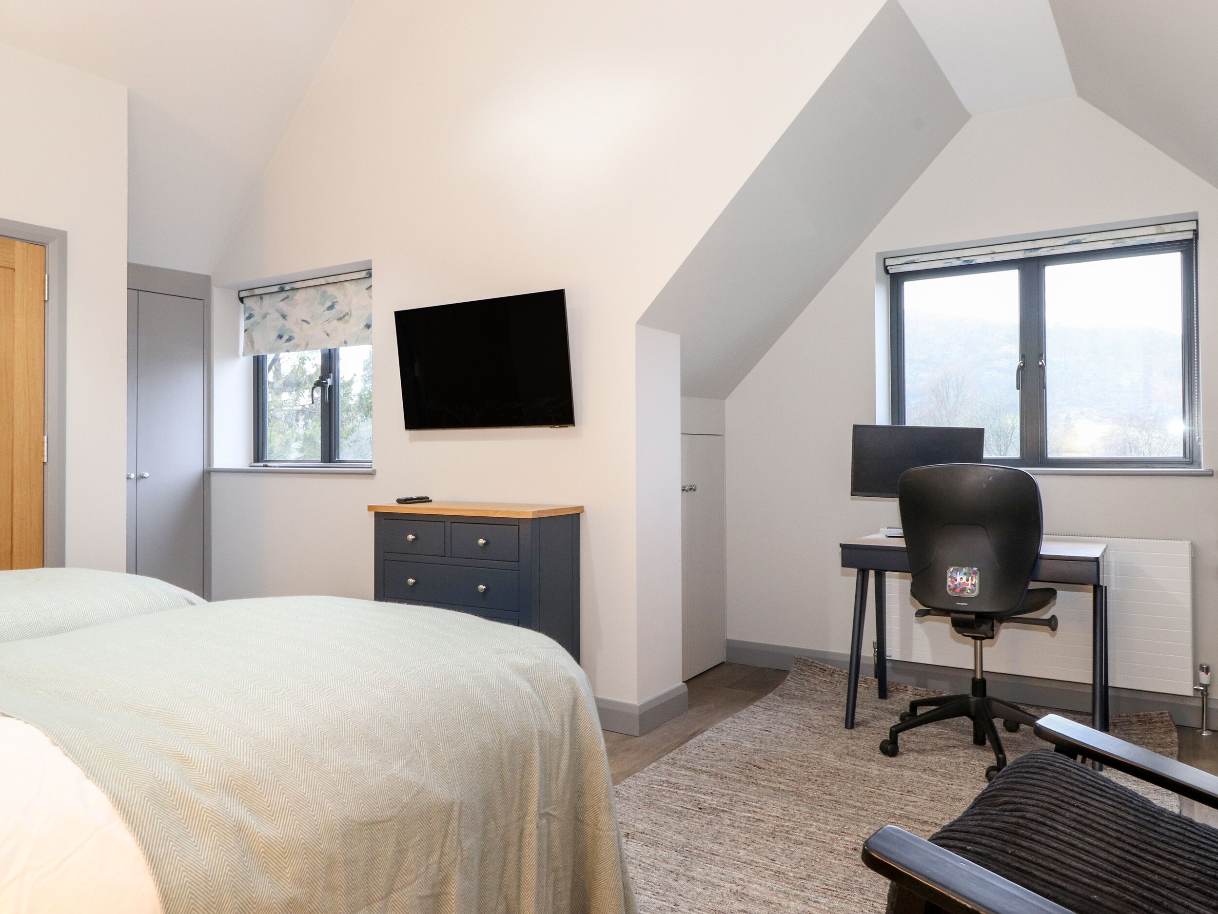 Un dormitorio con una cama, un escritorio, una silla, un televisor y una ventana.