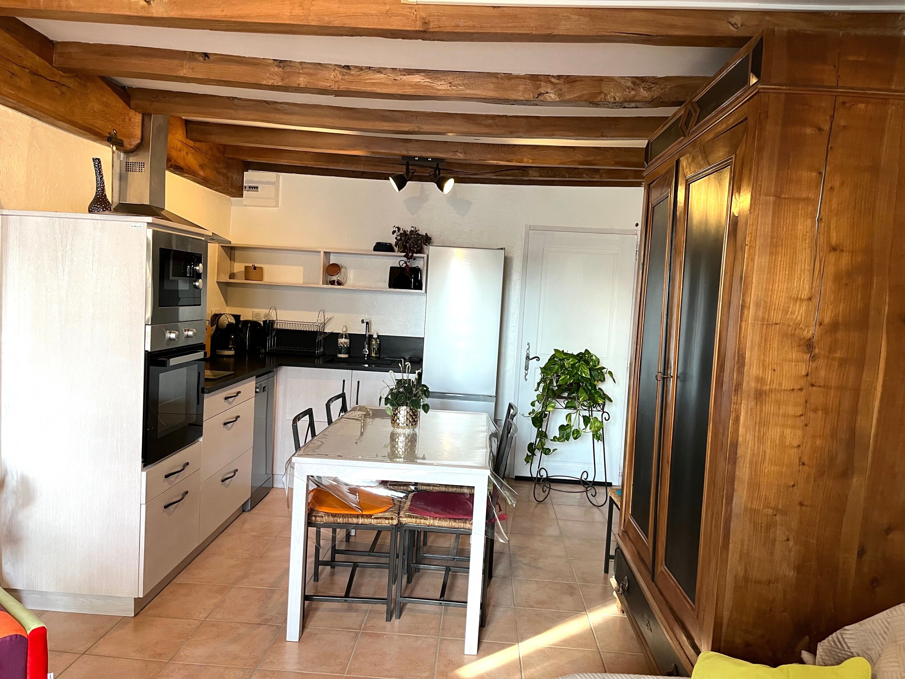 A kitchen with wooden beams, a dining table with chairs, a refrigerator, and a sink.