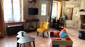 A rustic interior with exposed wooden beams, a stone wall, a television, a bench, a yellow armchair, a colorful sofa, and a tiled floor. - Cottage 'La Cassine' with Shared Terrace, Shared Garden and Wi-Fi (Taillant)