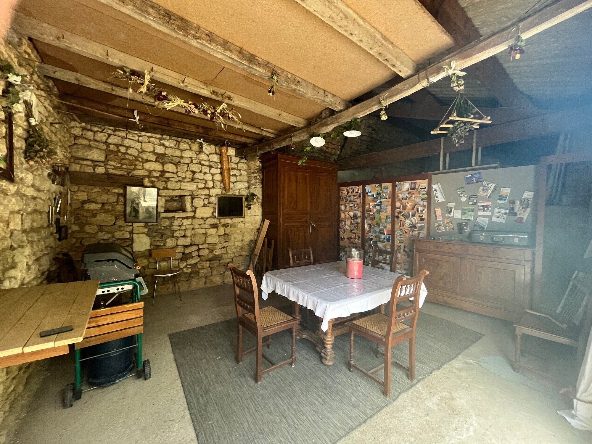 A rustic dining area with a stone wall, wooden ceiling beams, a table with chairs, and a refrigerator covered in photos.