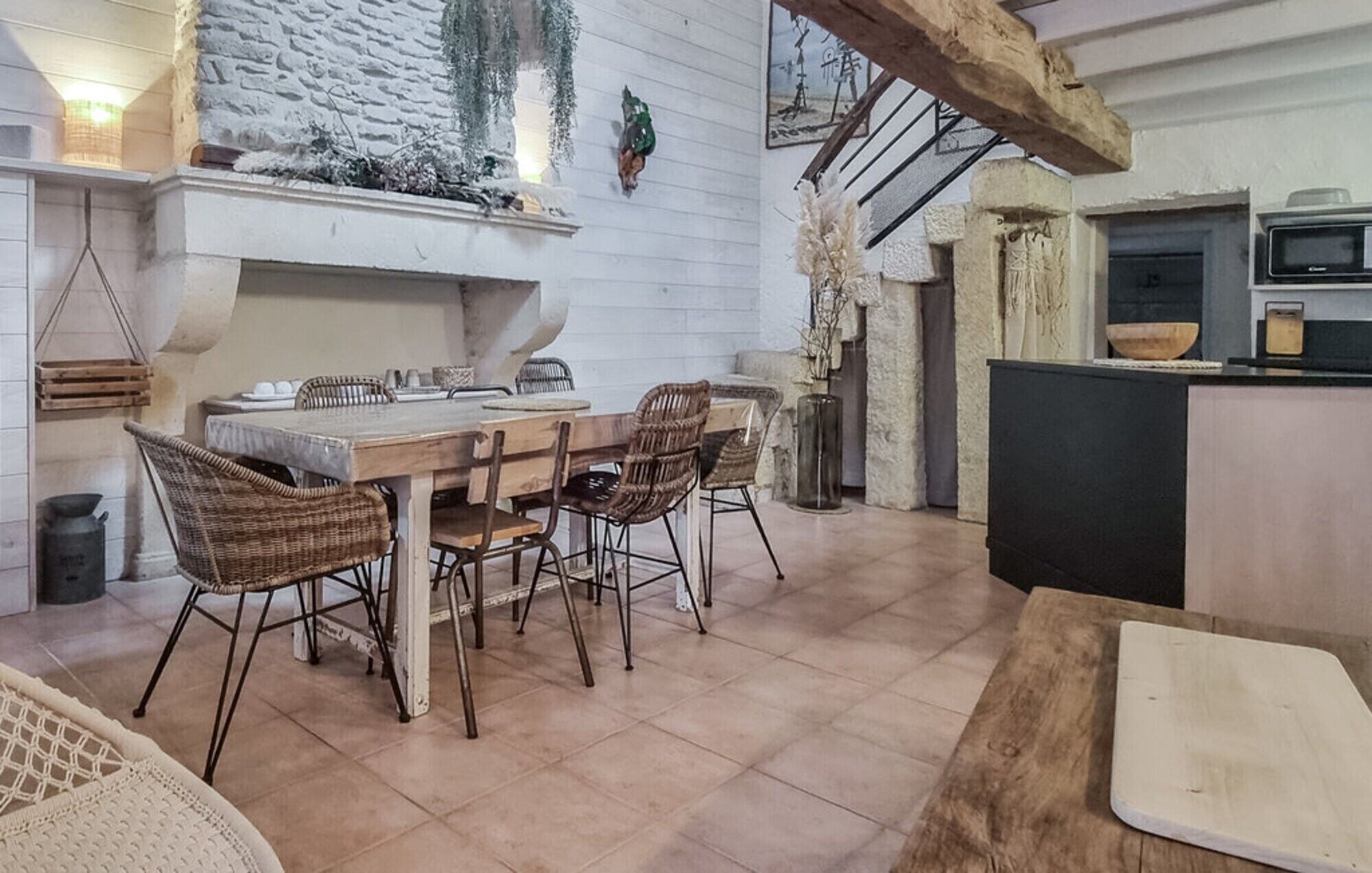 A rustic kitchen with a stone fireplace, wooden dining table, wicker chairs, and a modern microwave.