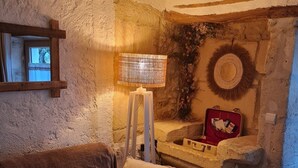 Ein rustikaler Raum mit einer Steinwand, einem Holzrahmenfenster, einer gewebten Lampe, einem roten Koffer und einem gewebten Kissen auf einer braunen Couch.