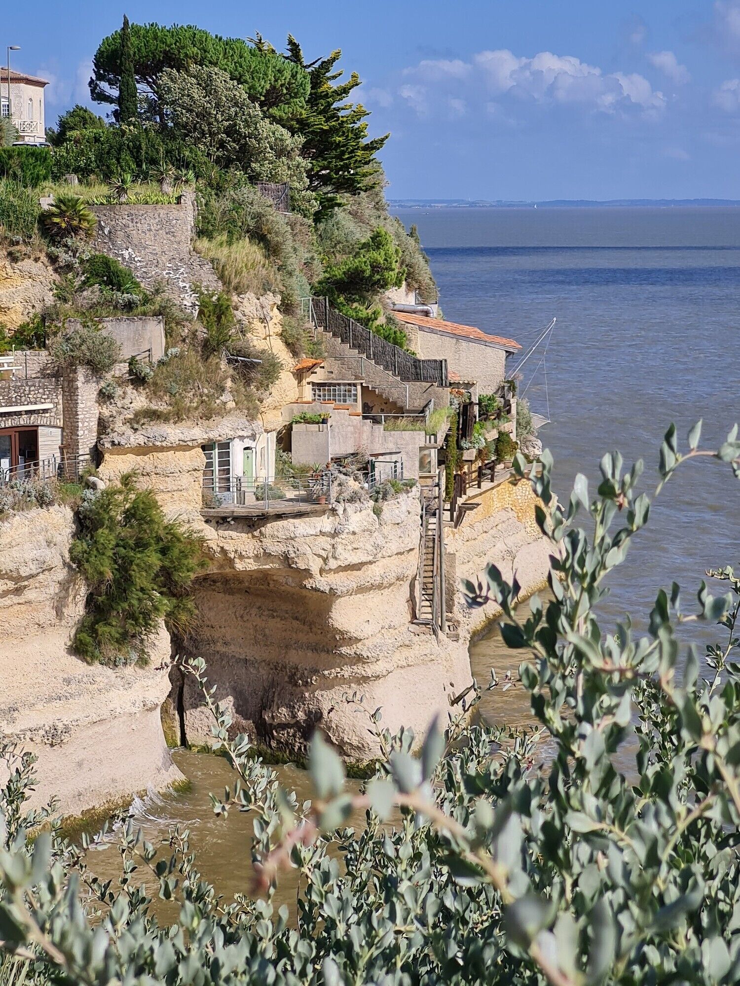 Un bâtiment situé sur la côte, avec des murs en pierre, un escalier et une vue sur la mer.