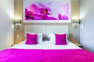 A hotel room with a large bed, two pillows, a headboard, and wall-mounted lights.