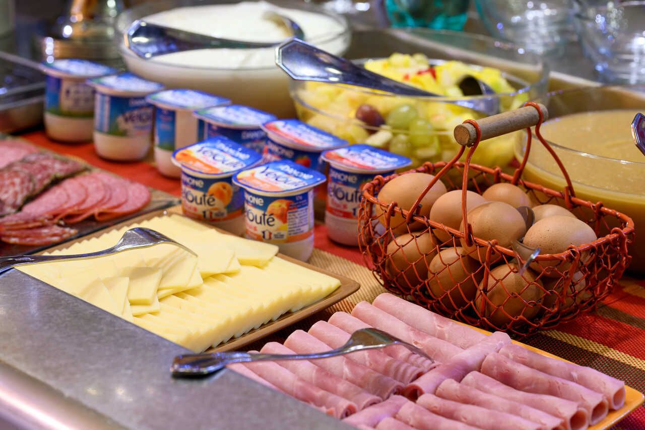 Un bufé con diferentes opciones de comida, incluyendo queso, jamón, huevos y yogur.