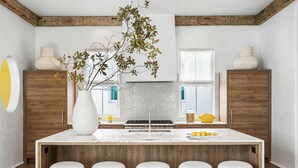 A modern kitchen with a central island, wooden cabinets, and a large window. - Official 30A Show House with Private Pool, Elevator, Putt Putt, Private Beach (Rosemary Beach)