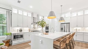 A modern kitchen with white cabinetry, a central island with bar stools, stainless steel appliances, and pendant lighting. - Private Pool, LSV/Golf Cart, Bikes, BRAND NEW! Walk to Beach in Blue Mountain! (Santa Rosa Beach)