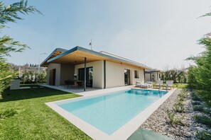 Et moderne hus med swimmingpool, overdækket terrasse og velplejet græsplæne.