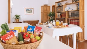 En morgenmadsbuffet med et varieret udvalg af mad og drikke, en reol og en potteplante.