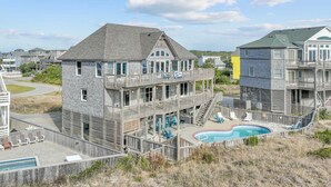 A multi-story building with a pool and outdoor seating. - Oceanfront w/ Pool, Hot Tub, Elevator, Game Room. Feel like an Island Princess! (Frisco)