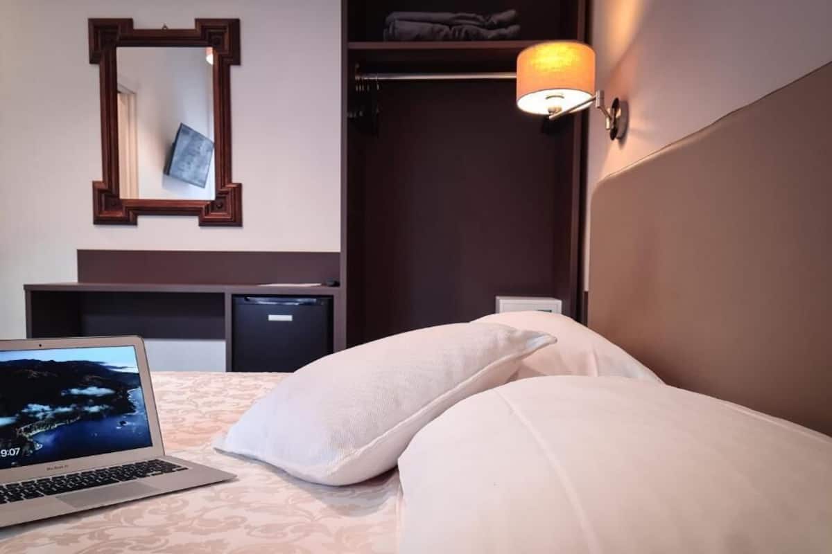 Hotelkamer met een bed, een laptop, een bedlamp, een kledingkast en een spiegel.
