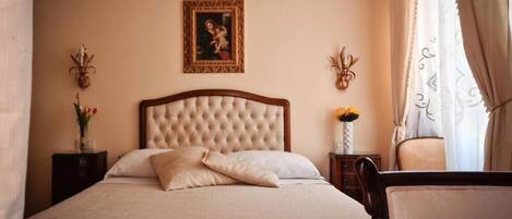 A neatly made bed with a tufted headboard, a bedside table with a vase of flowers, and a wall-mounted picture.