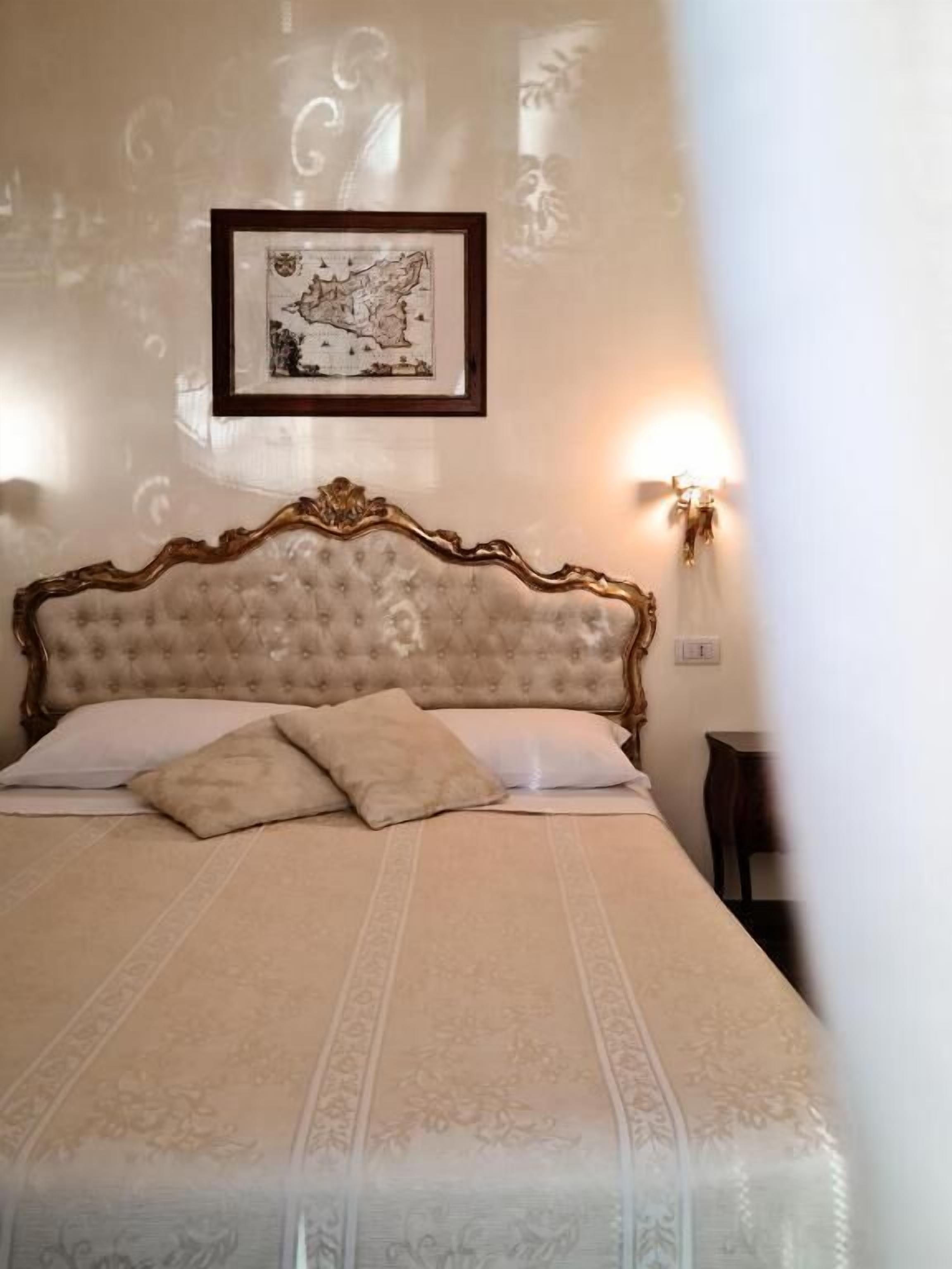 Una cama bien hecha con cabecera capitonada, un mapa enmarcado en la pared y una lámpara de pared.