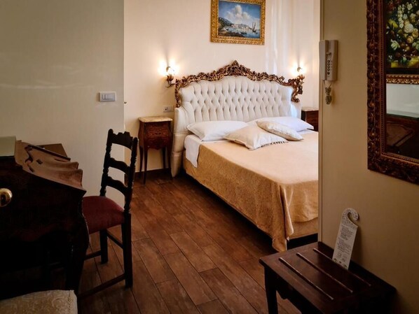 A bedroom with a large bed, a wooden chair, a nightstand, and a painting on the wall.