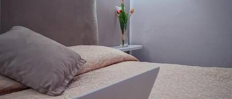 A bed with a tufted headboard, a laptop on the bed, and a bedside table with a vase of flowers.