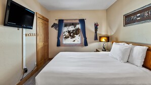 Ein Hotelzimmer mit Bett, Wandfernseher, Fenster mit Vorhängen und einem Holz-Kopfteil.