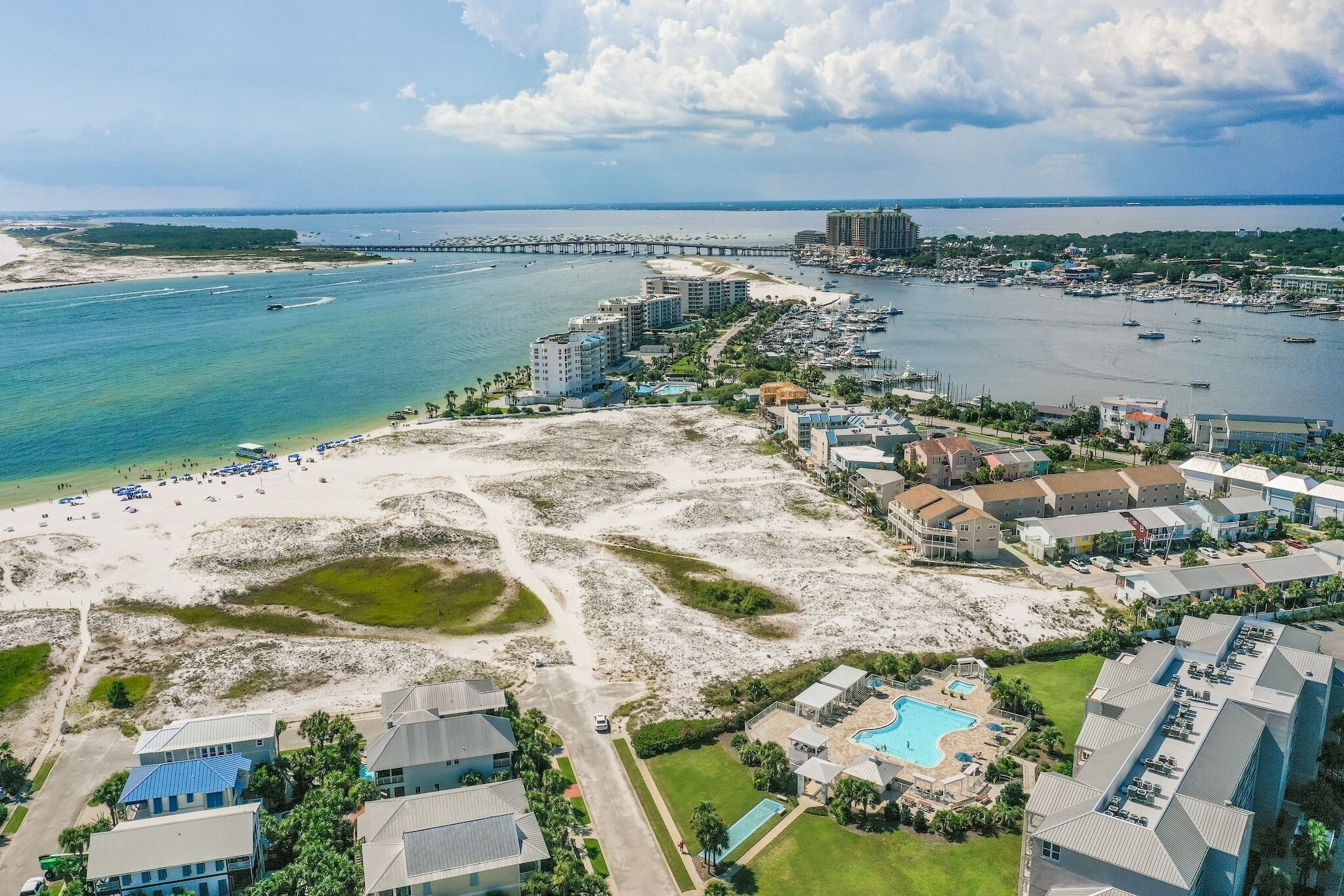 An aerial view of a coastal resort with beachfront properties, a marina, and a bridge in the background.