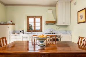 A kitchen with a wooden dining table, white cabinets, a window, and a gas stove. - Agriturismo "Podere San Bartolo - Fienile" with Shared Pool, Private Terrace and Wi-Fi (Barberino Val D'elsa)