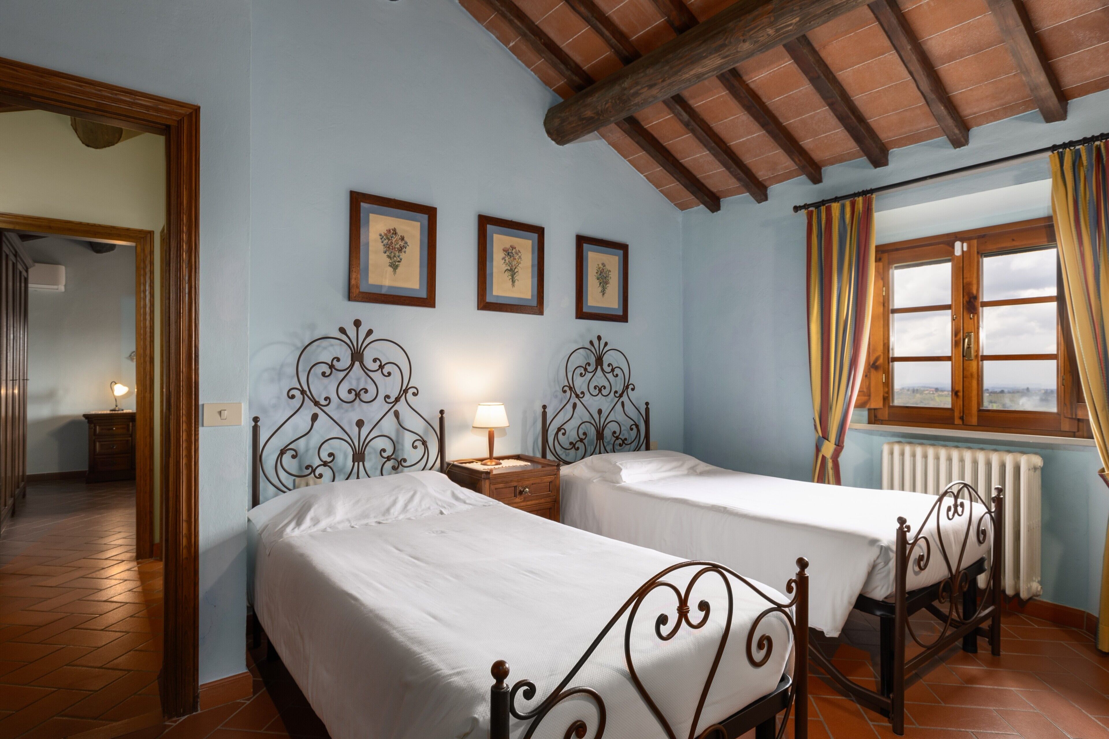Una camera da letto con due letti, soffitto in legno e finestra con tende.
