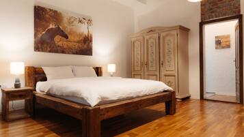 A bedroom with a wooden bed, two bedside tables, a large wall-mounted painting, a cabinet, and a door leading to another room.