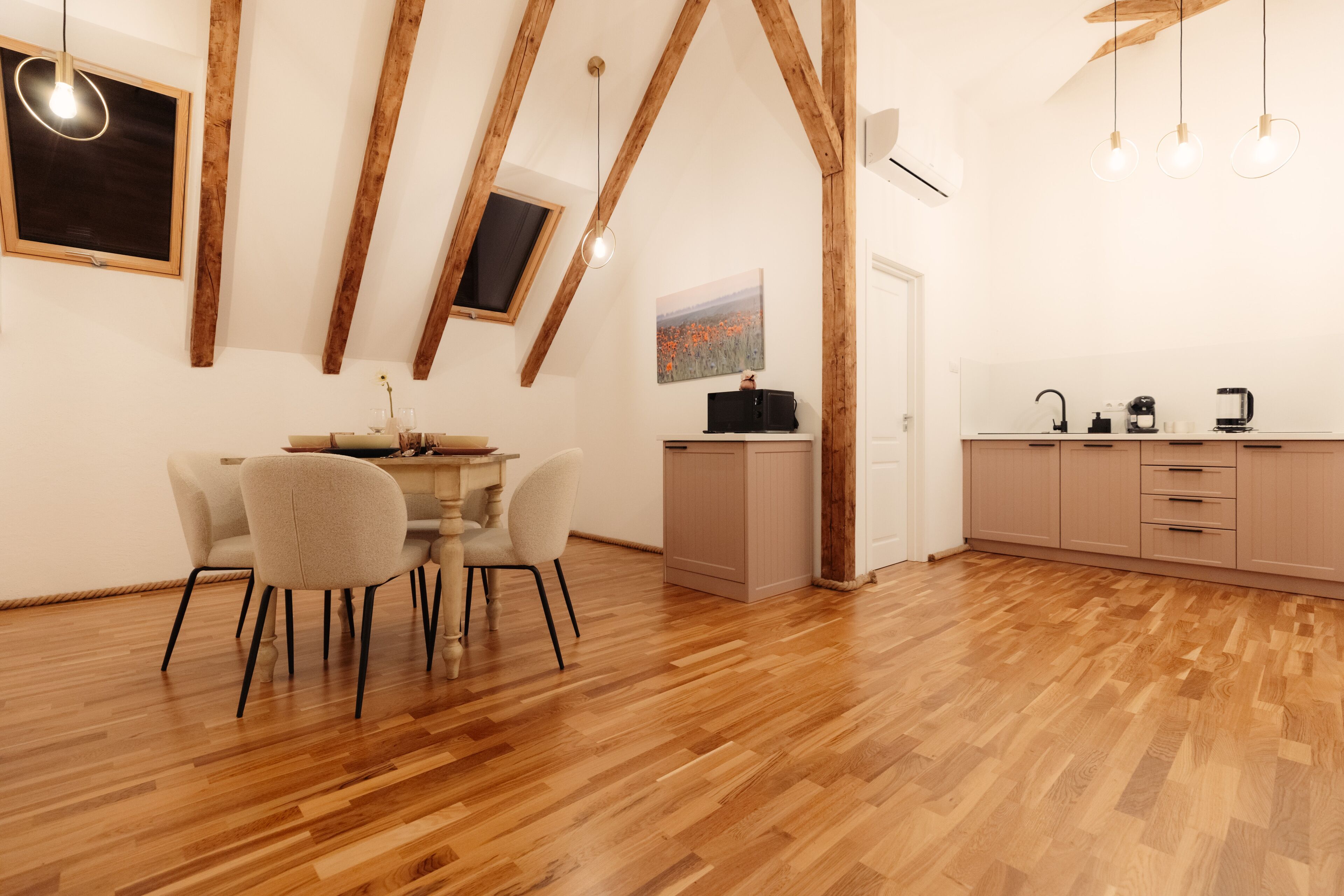Een moderne keuken met houten balken, een eethoek met tafel en stoelen, en uitzicht op de omgeving door een raam.