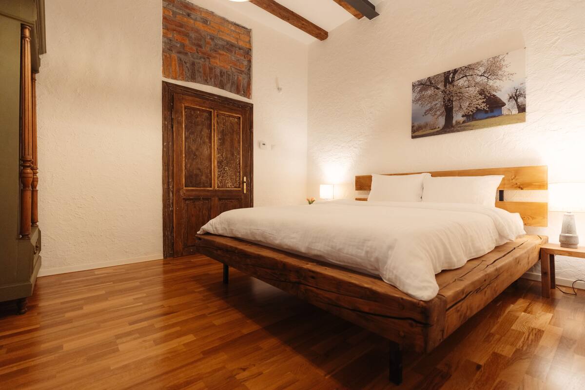 A bedroom with a wooden bed, a brick wall, and a painting.