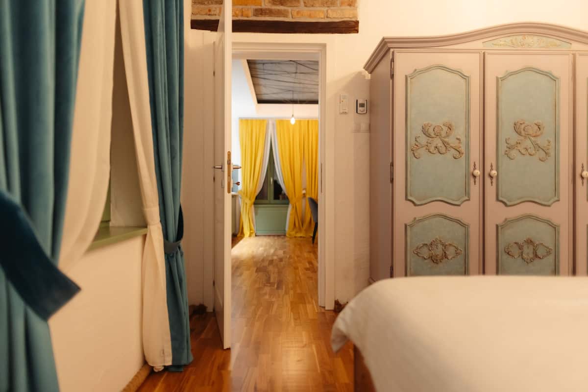 A hallway leading to a bedroom with a wooden floor, a bed, and a wardrobe with decorative panels.