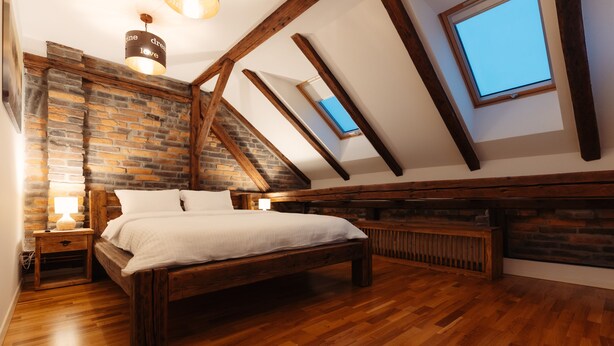 Une chambre avec un lit en bois, un mur en briques et une lucarne.