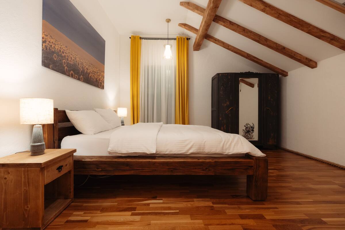 A bedroom with a wooden bed, a nightstand, a lamp, and a painting on the wall.
