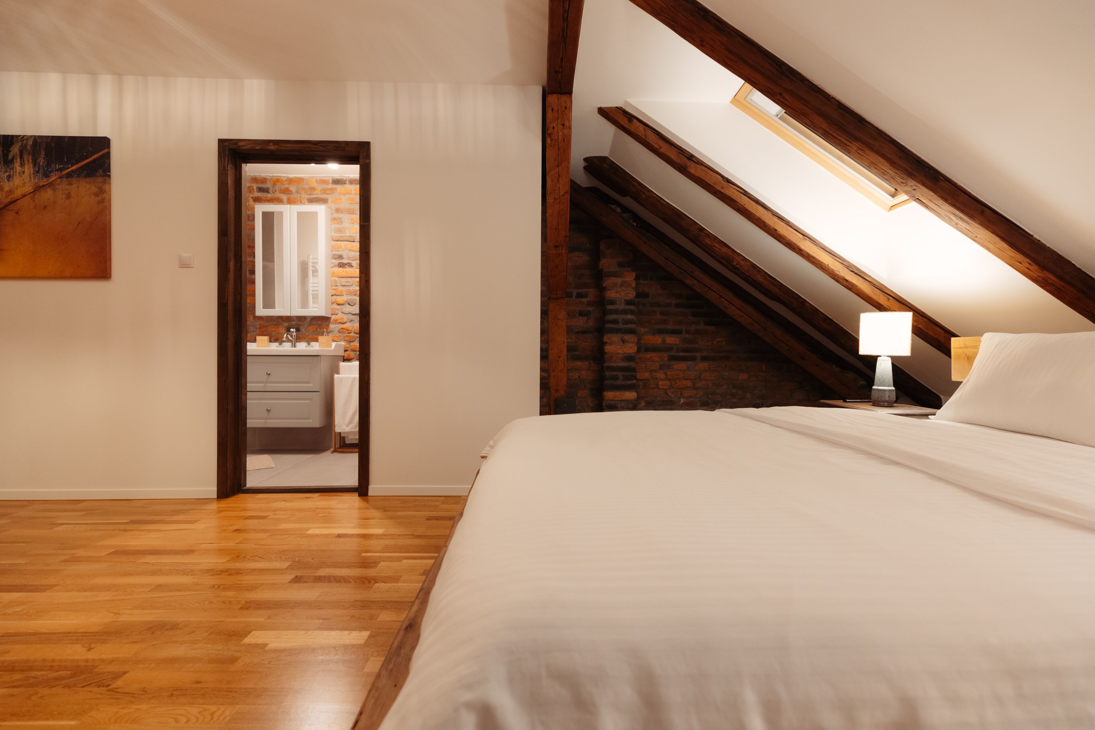 Un dormitorio con techo de madera, un tragaluz, una cama y una mesita de noche con lámpara.