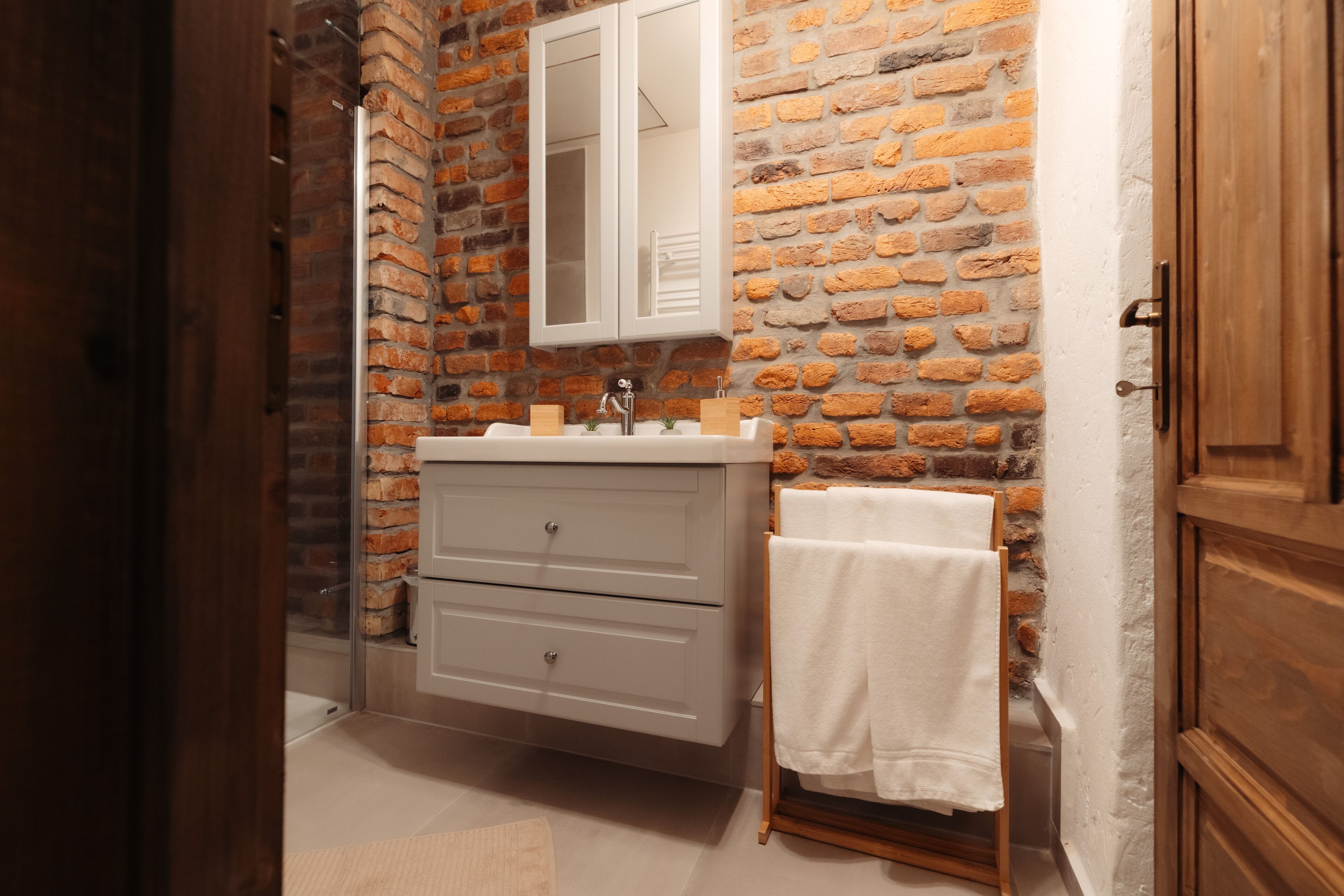 Une salle de bain avec un mur en briques, un meuble-lavabo blanc, un miroir et un porte-serviettes.