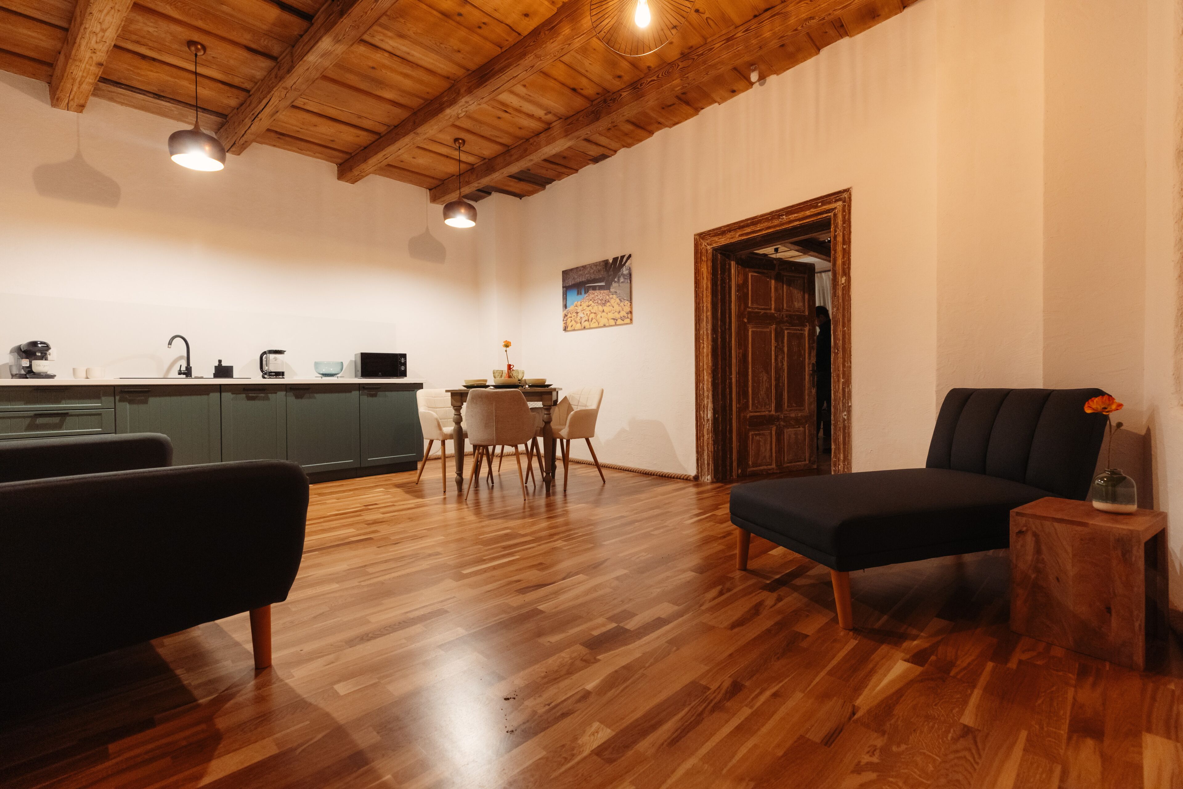A cozy living room with a wooden ceiling, a dining area with a table and chairs, and a kitchen with cabinets and appliances.