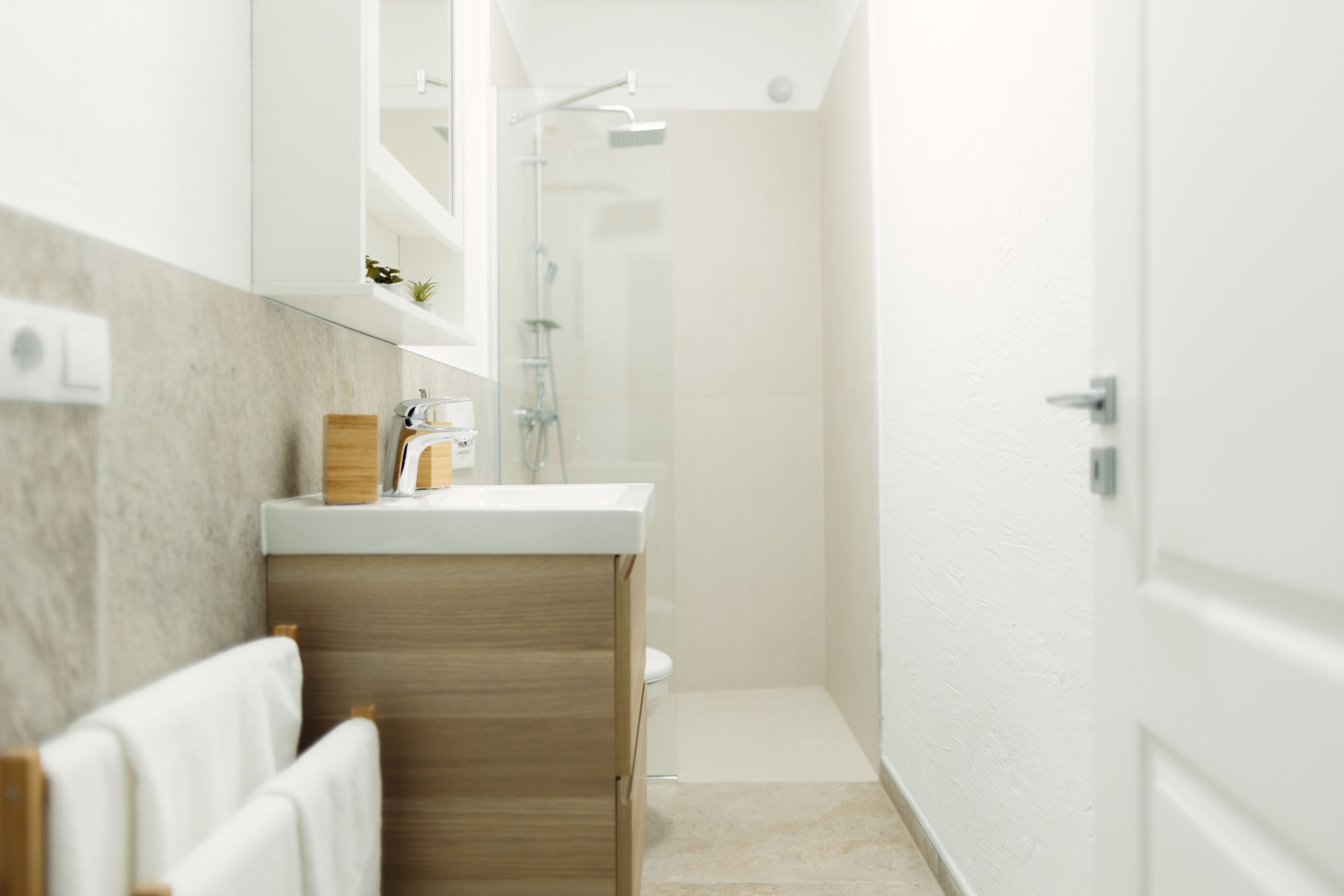 A modern bathroom with a wooden vanity, a glass shower enclosure, and a white door.