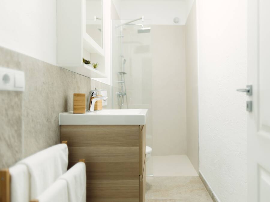 A modern bathroom with a wooden vanity, a glass shower enclosure, and a white door.