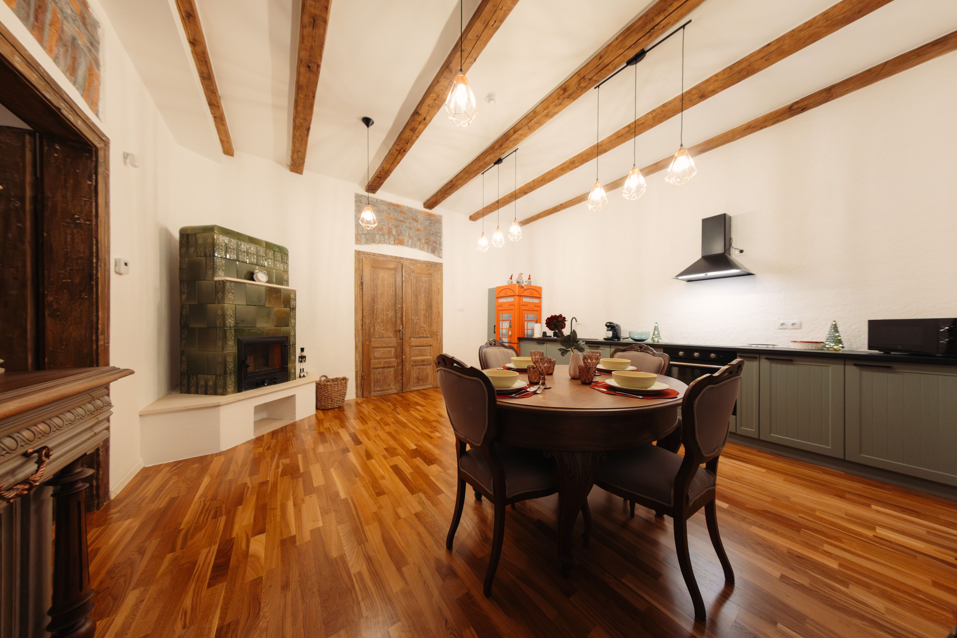 A dining area with a wooden table and chairs, a fireplace, and a kitchen in the background.