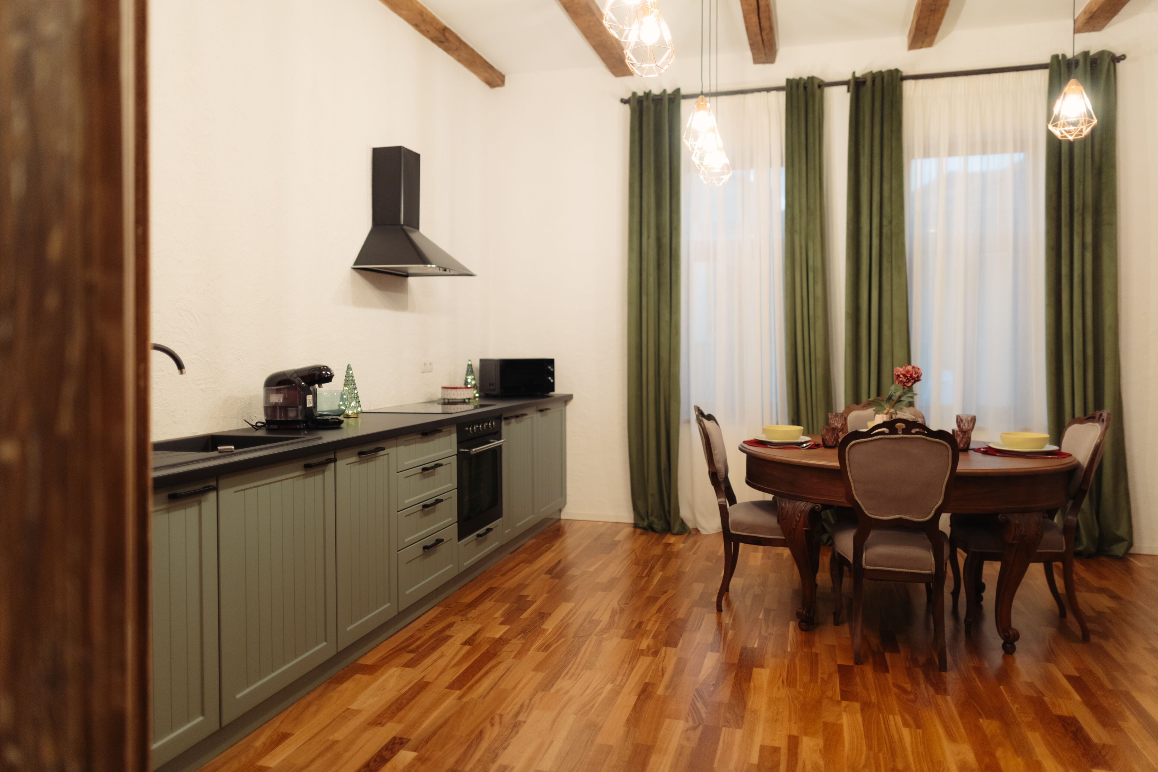 Una cocina con armarios grises, una campana extractora negra y una zona de comedor con una mesa y sillas de madera.
