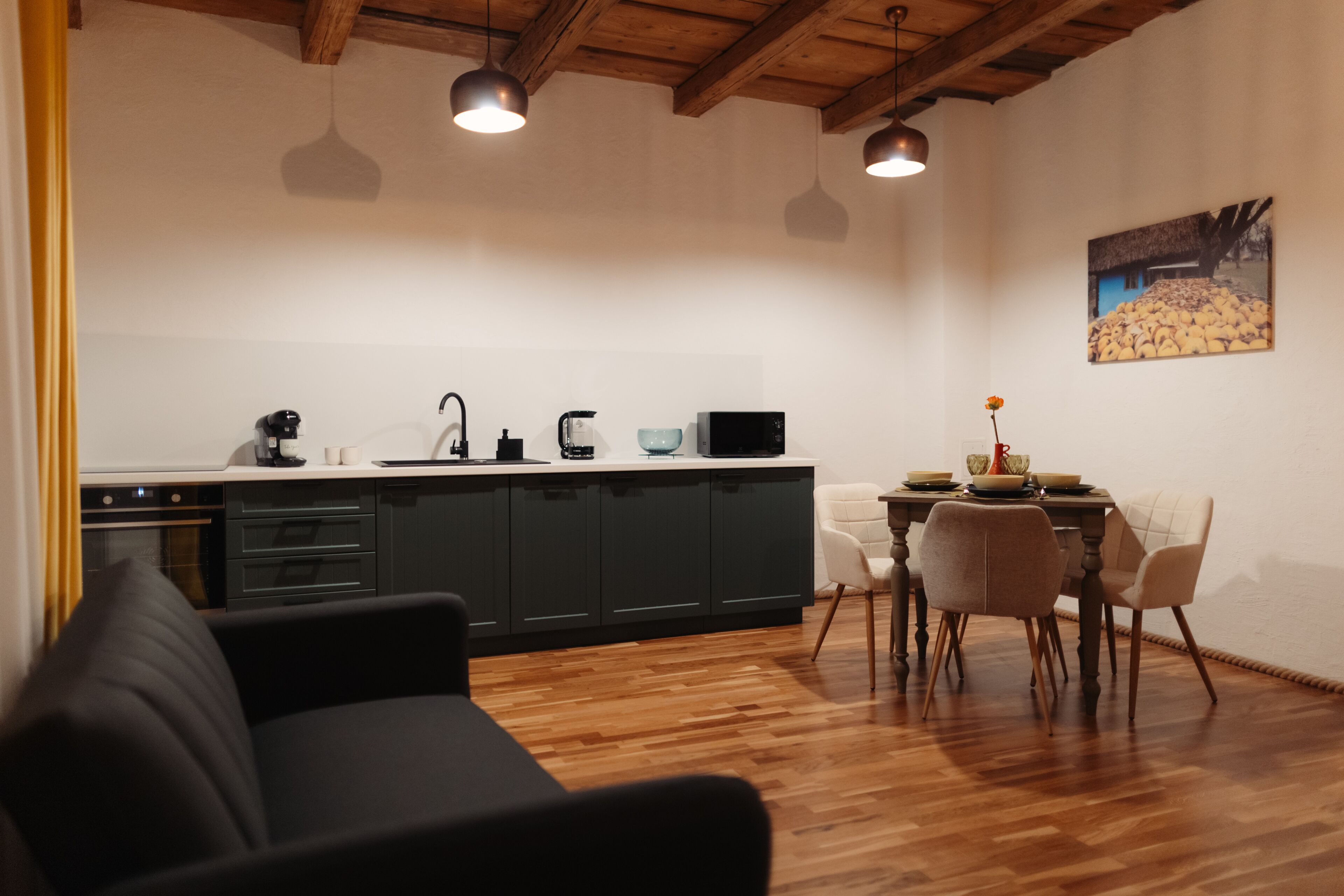 Cozinha moderna com armários escuros, uma mesa de jantar com cadeiras e luminárias pendentes.