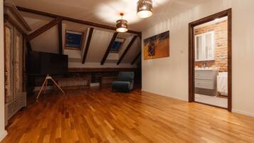Une chambre spacieuse aménagée en mezzanine, avec un plancher en bois, des poutres apparentes, une grande fenêtre et une vue sur la salle de bain.