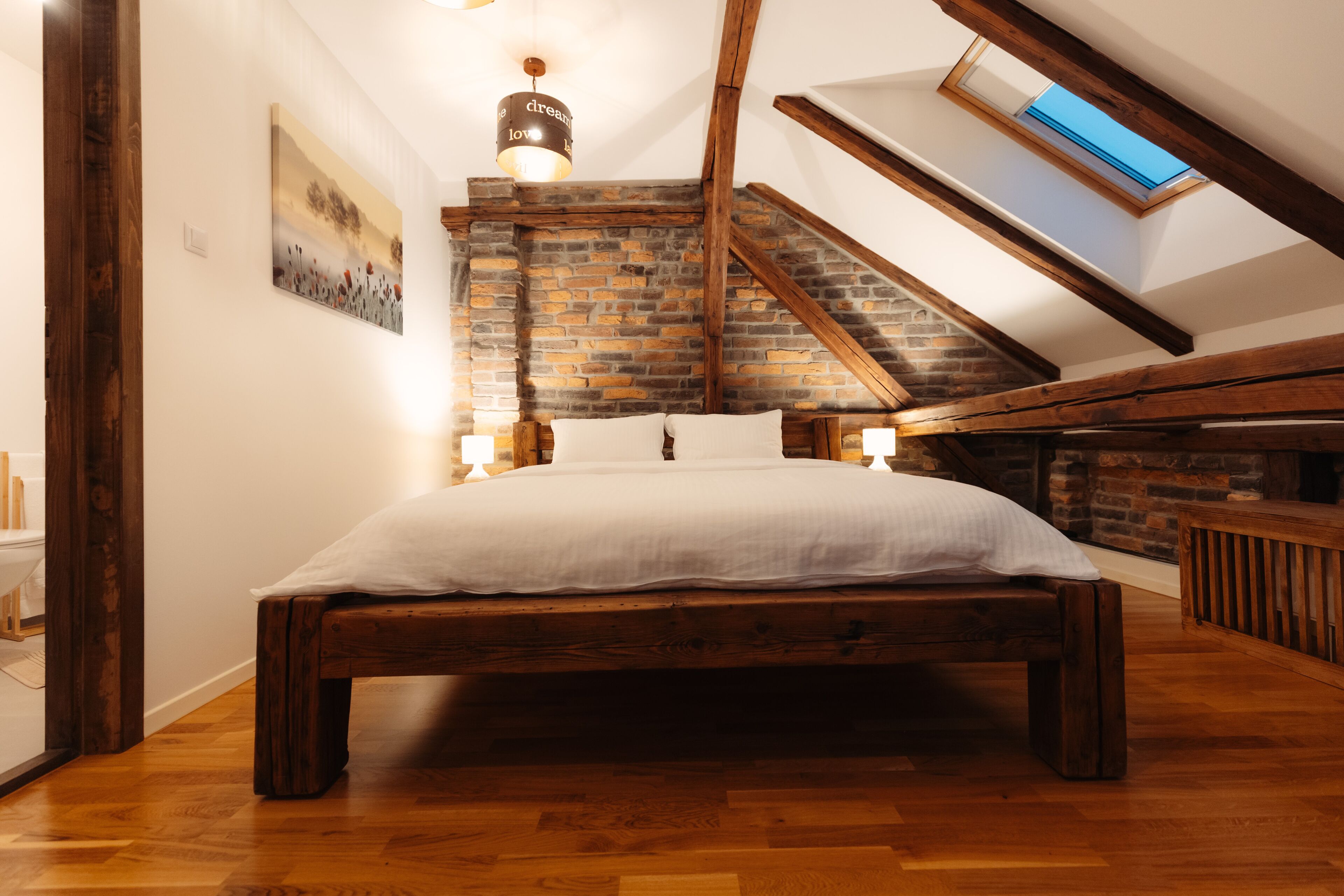 A bedroom with a sloped ceiling, exposed brick walls, a wooden bed, and a skylight.