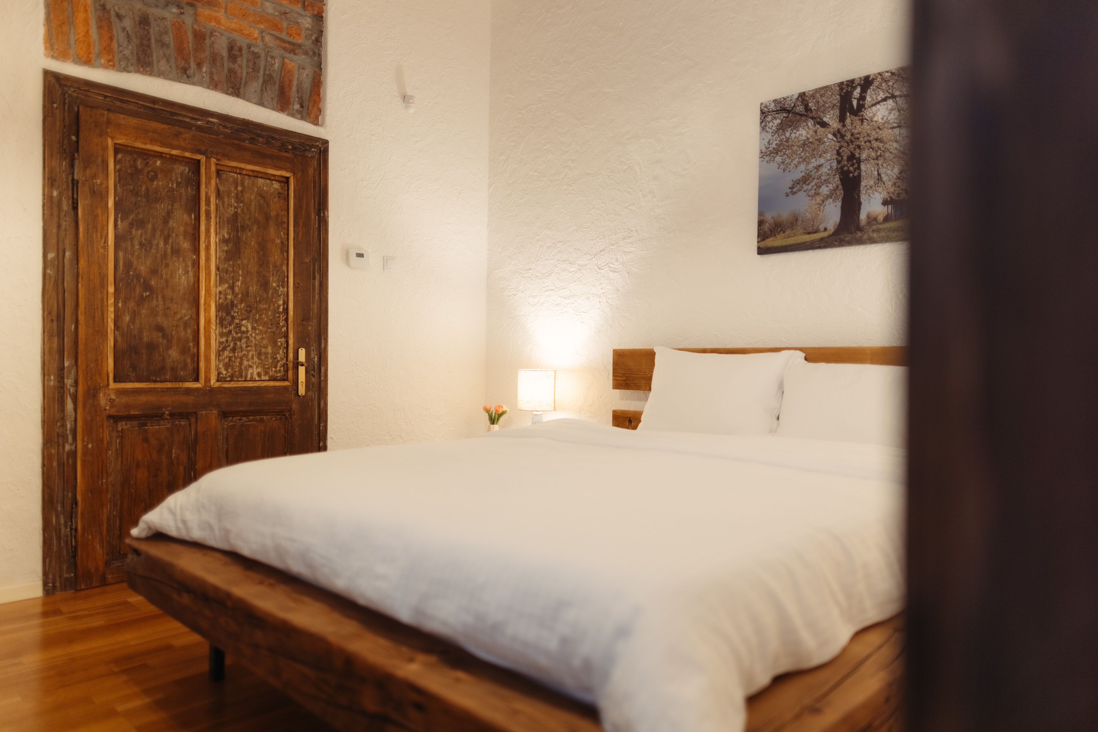 Une chambre à coucher avec un lit en bois, une table de chevet avec une lampe et une porte surmontée d’un mur en briques.