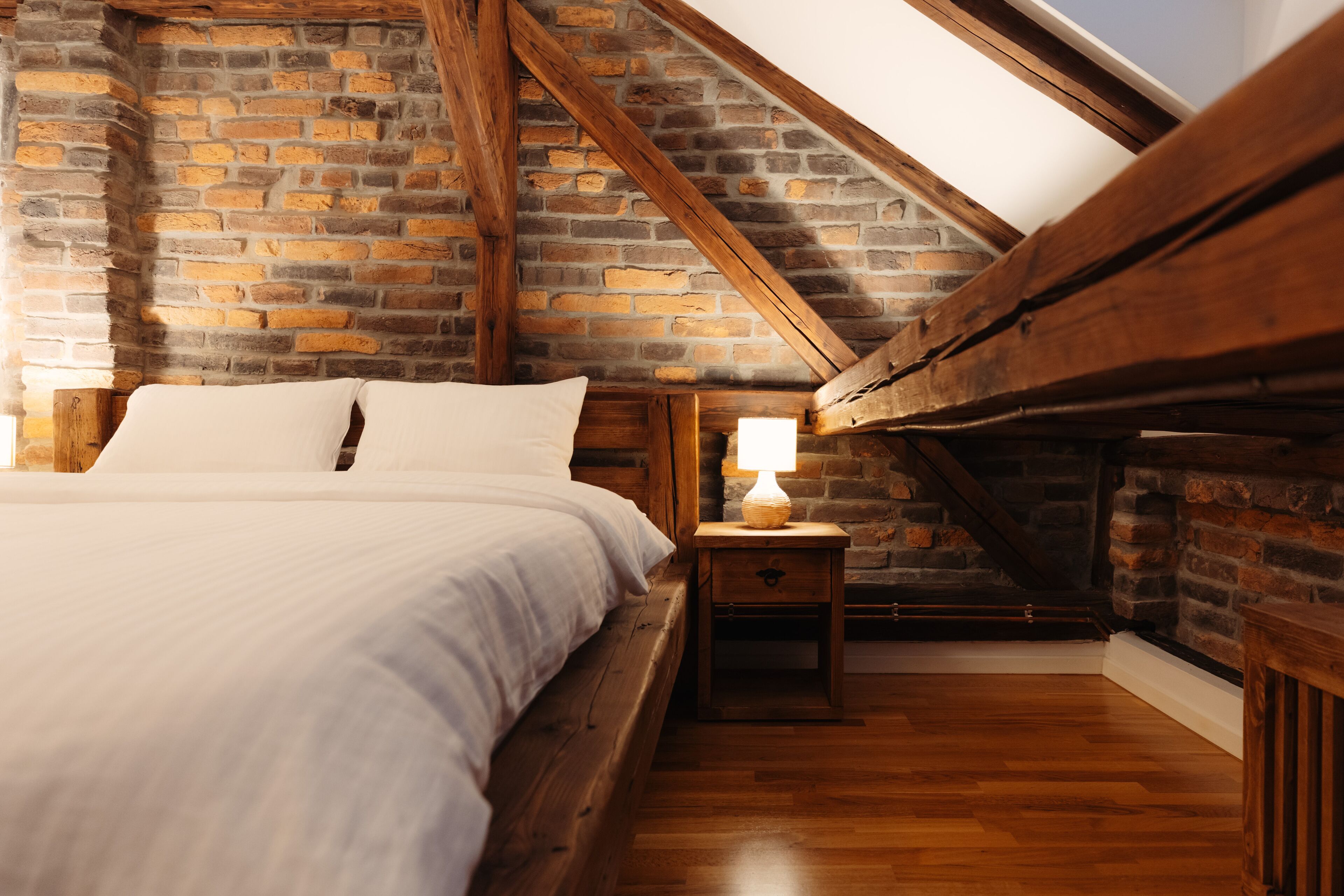 A bedroom with a wooden bed, a nightstand, and a brick wall.
