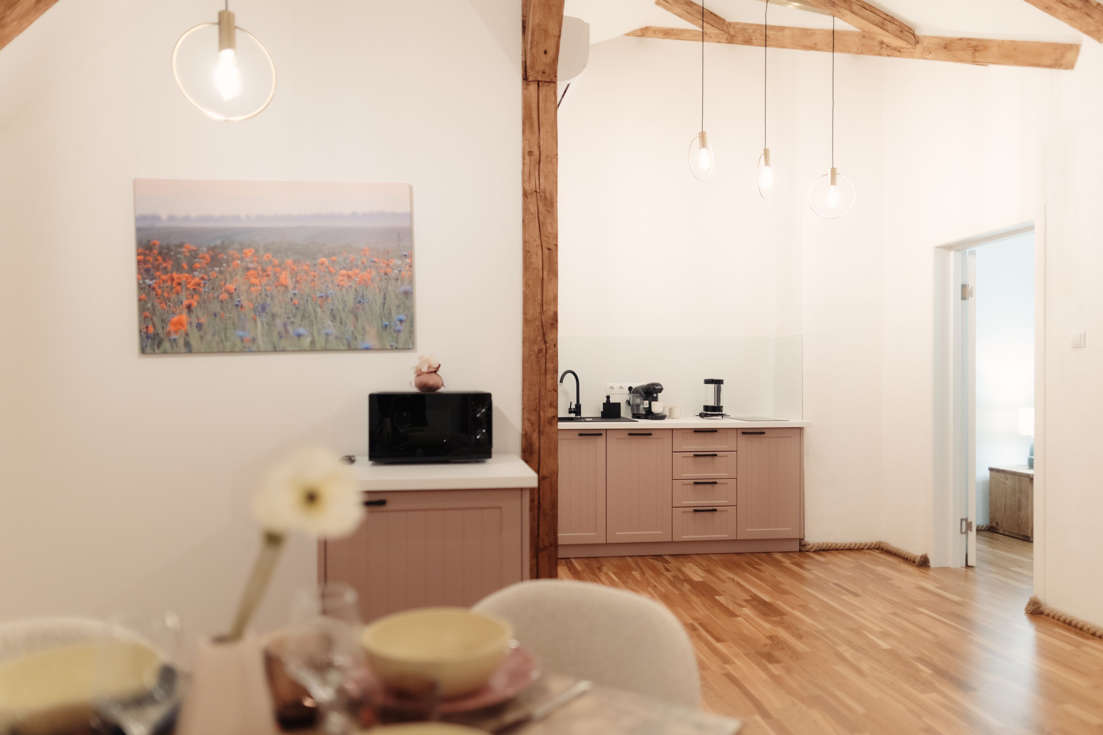 Cozinha moderna com vigas de madeira, área de jantar com mesa posta para dois e vista para um campo pela janela.
