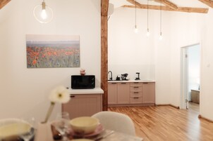 A modern kitchen with wooden beams, a dining area with a table set for two, and a view of a field through a window.