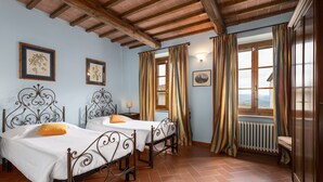 Una habitación con dos camas, vigas de madera, una ventana con cortinas y un radiador.