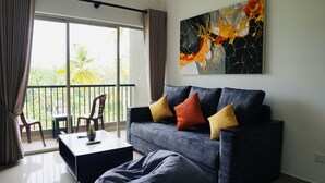 A modern living room with a grey sofa, colorful cushions, a small table with a plant, and a large abstract painting on the wall.