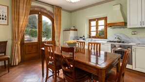 Un coin repas avec une table et des chaises en bois, une cuisine avec des meubles blancs et une vue à travers une porte.