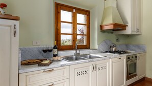 Une cuisine équipée d’un évier à deux bacs, de cadres de fenêtres en bois, d’une cuisinière à gaz et de meubles de rangement blancs.