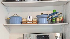 Una cocina con estufa negra, encimera de madera y repisas superiores con distintos utensilios de cocina.